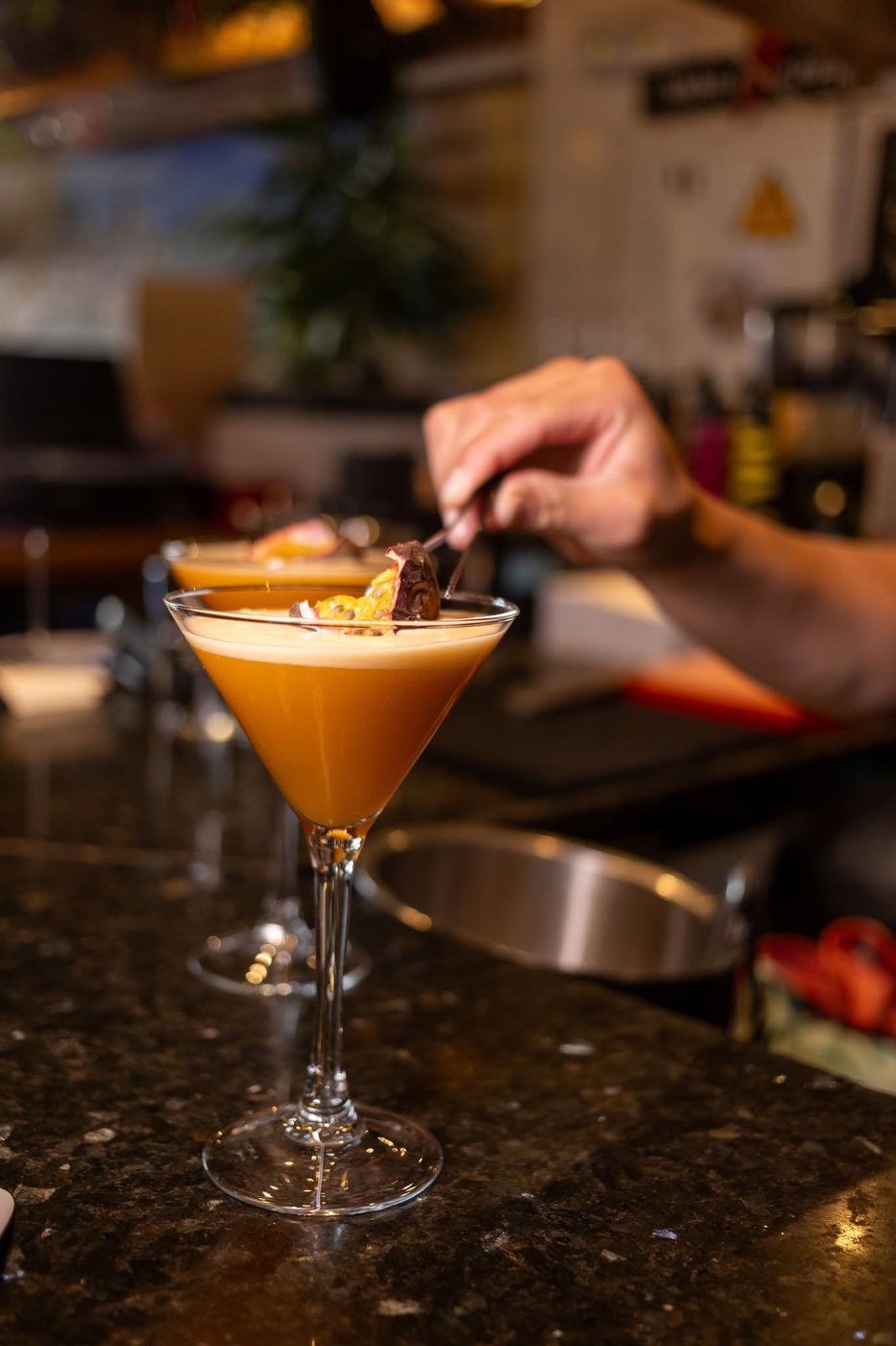A bartender garnishing two passion fruit martinis