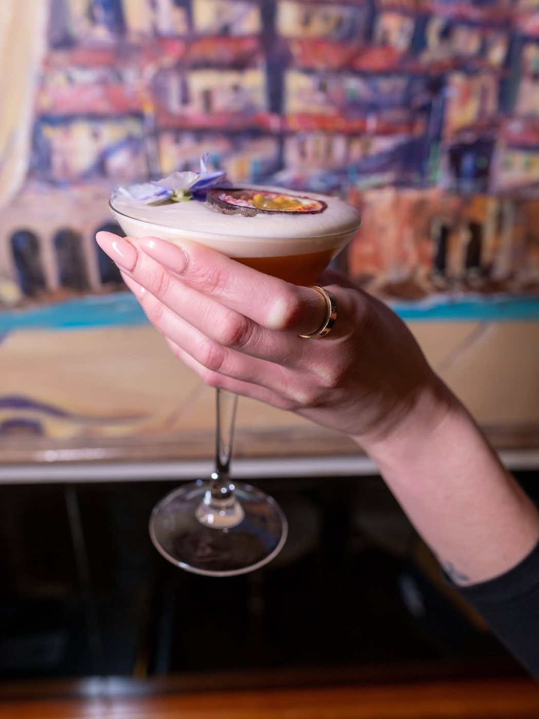 A cocktail held up against the painted Naples mural