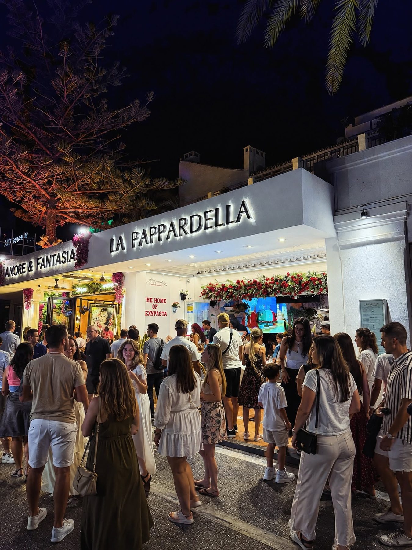 La Pappardella at night, a queue outside, the painted wall lit