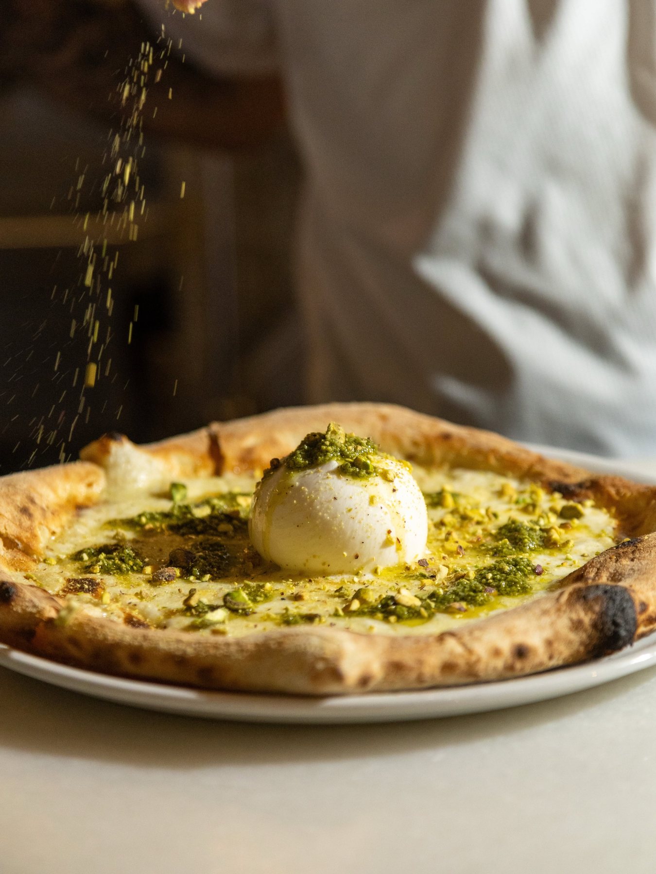Pizza Burrata — white base, mozzarella, pesto and pistachio, dusted at the pass