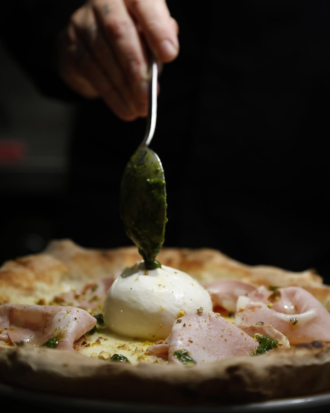 Pesto spooned onto a burrata and mortadella pizza