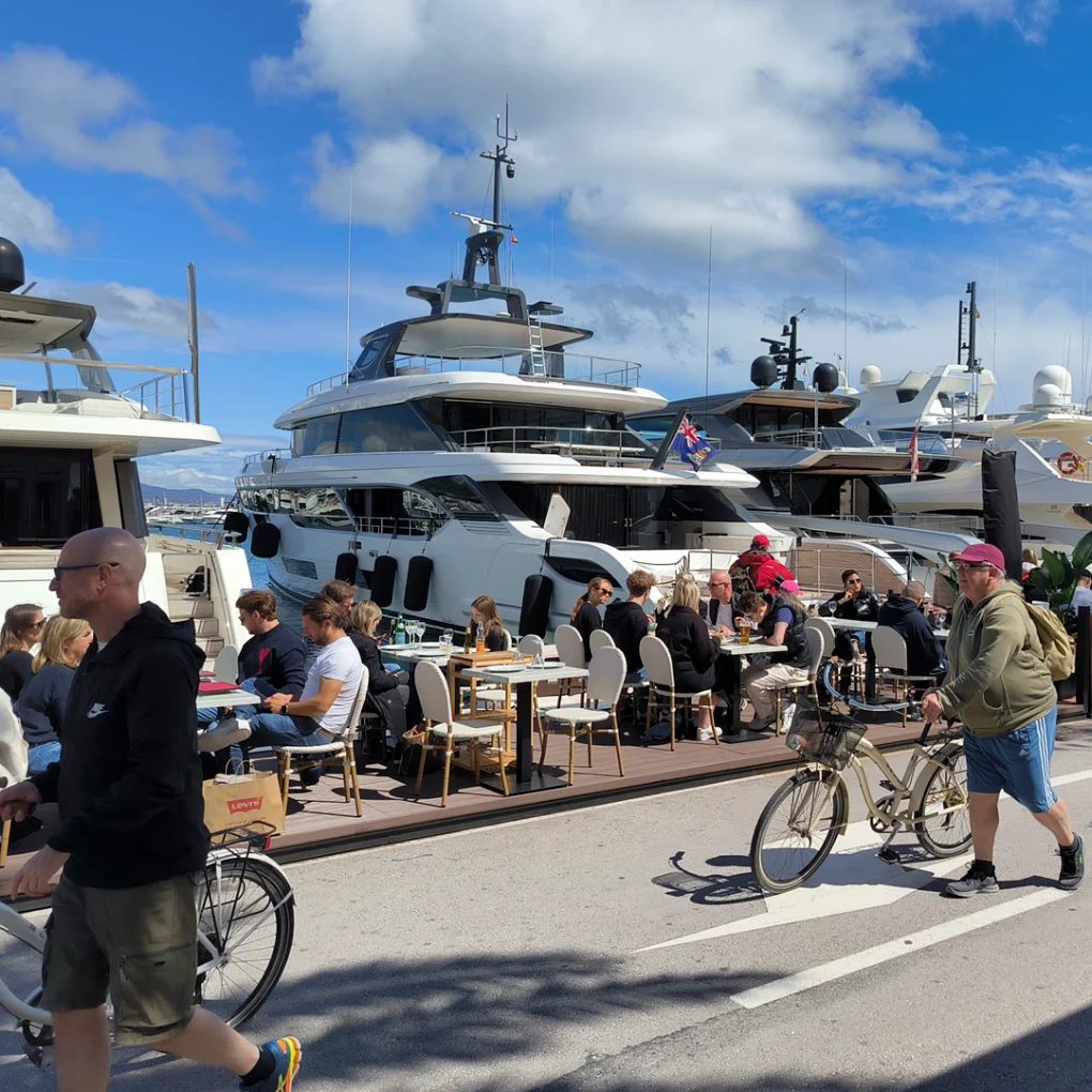 The Puerto Banús promenade outside the restaurant, diners on the deck, superyachts moored opposite