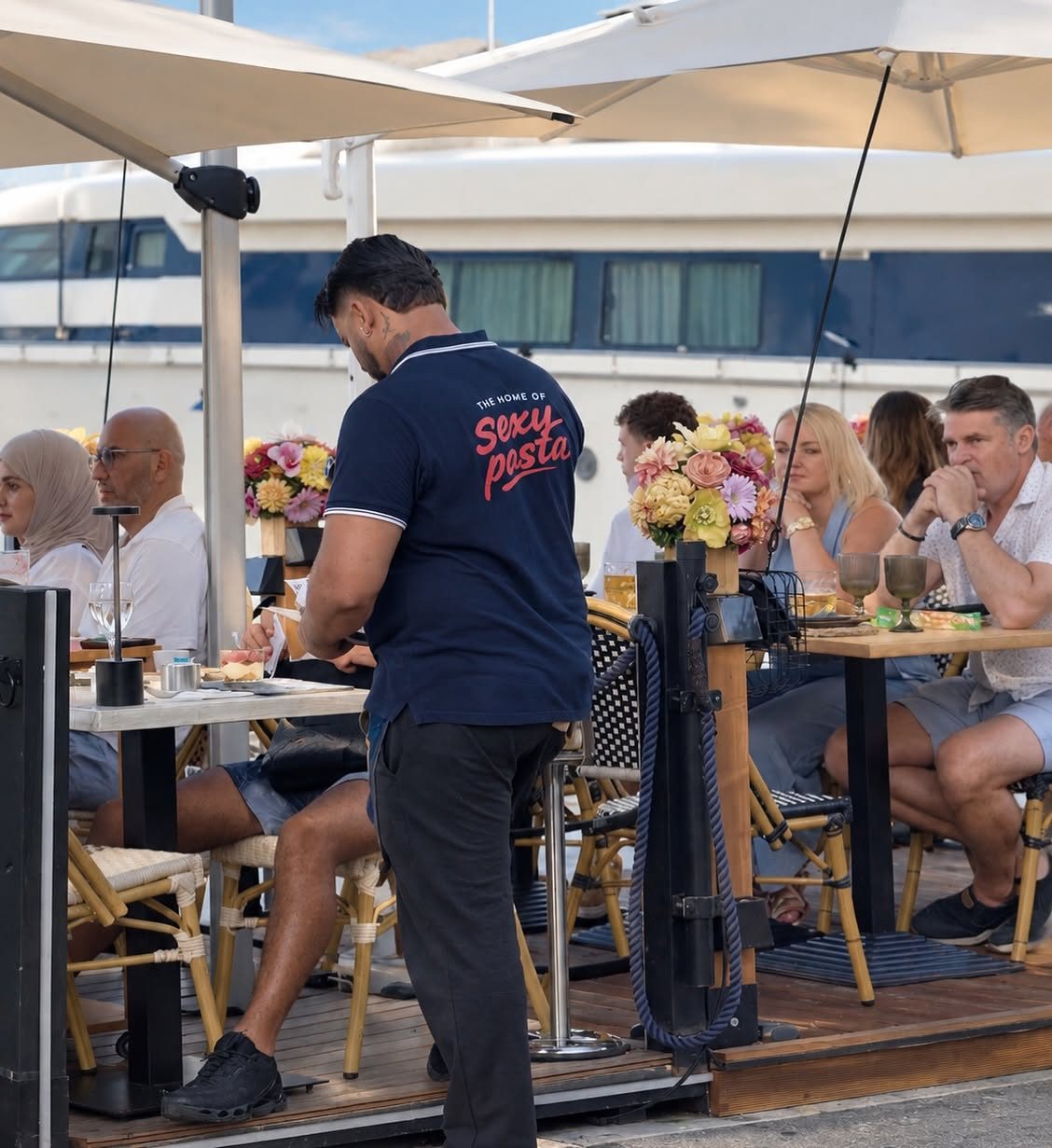 A waiter on the terrace in a navy polo reading The Home of Sexy Pasta