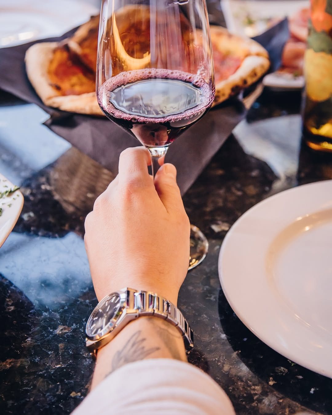 A glass of red wine raised over a pizza on the table